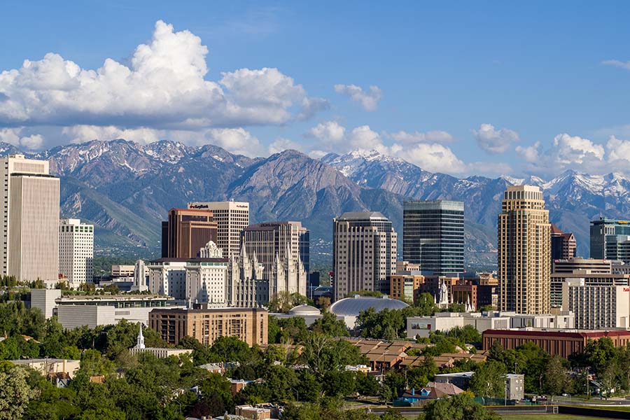 Contact - Commercial Buildings and Skyscrapers Surrounded by Green Foliage in Downtown Salt Lake City Utah with Mountains Against a Cloudy Blue Sky in the Background
