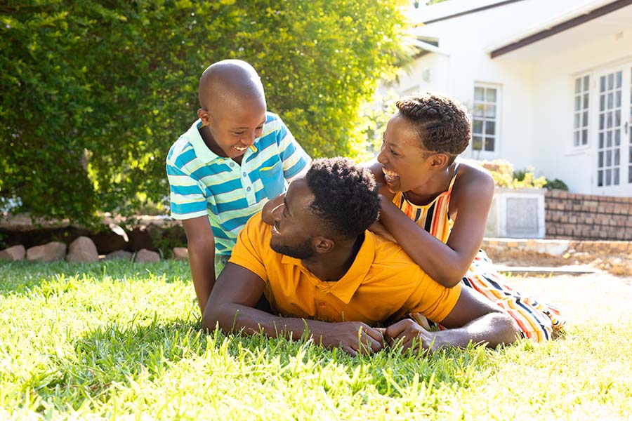 Personal Insurance - Portrait of a Cheerful Family with a Young Son Playing Together on the Green Grass in Their Backyard During a Warm Summer Day